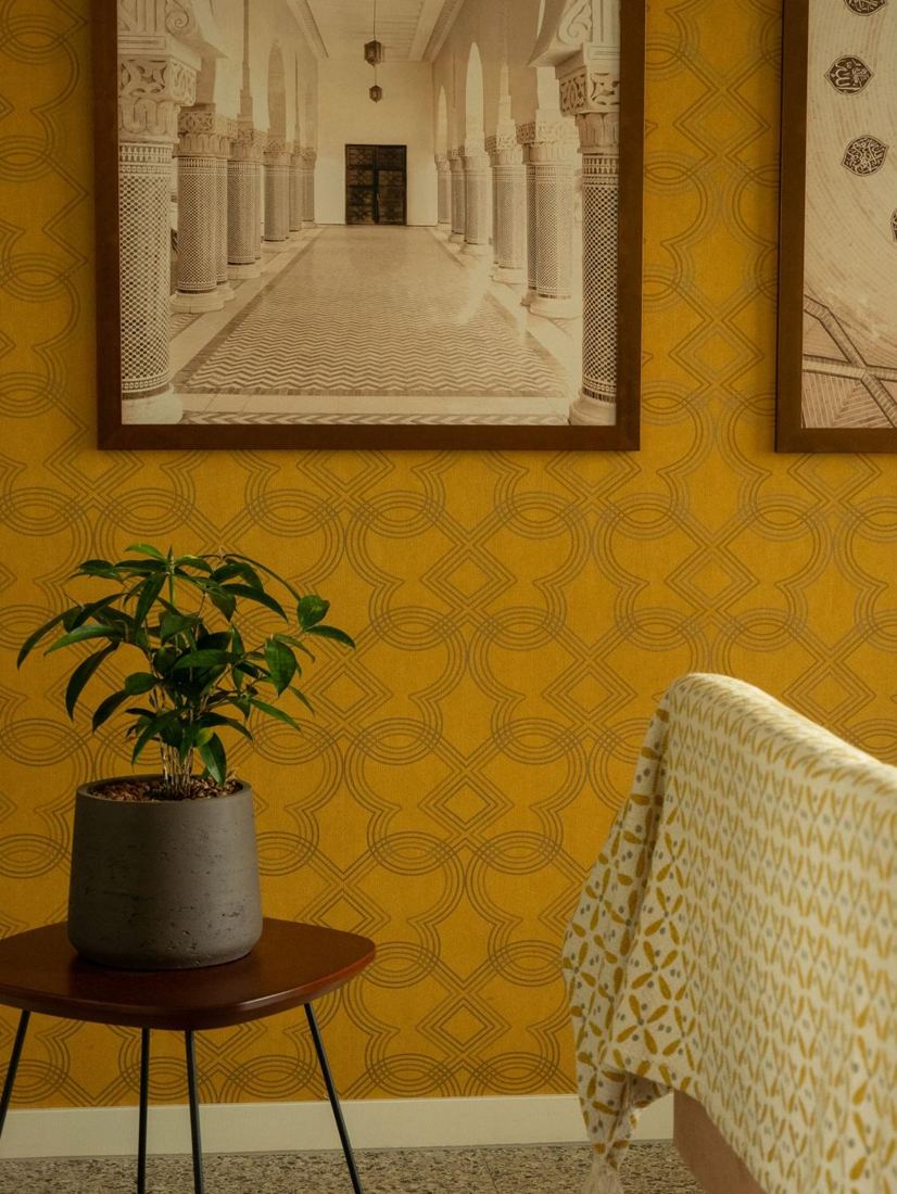 Mustard damask wallpaper behind a potted plant and side table